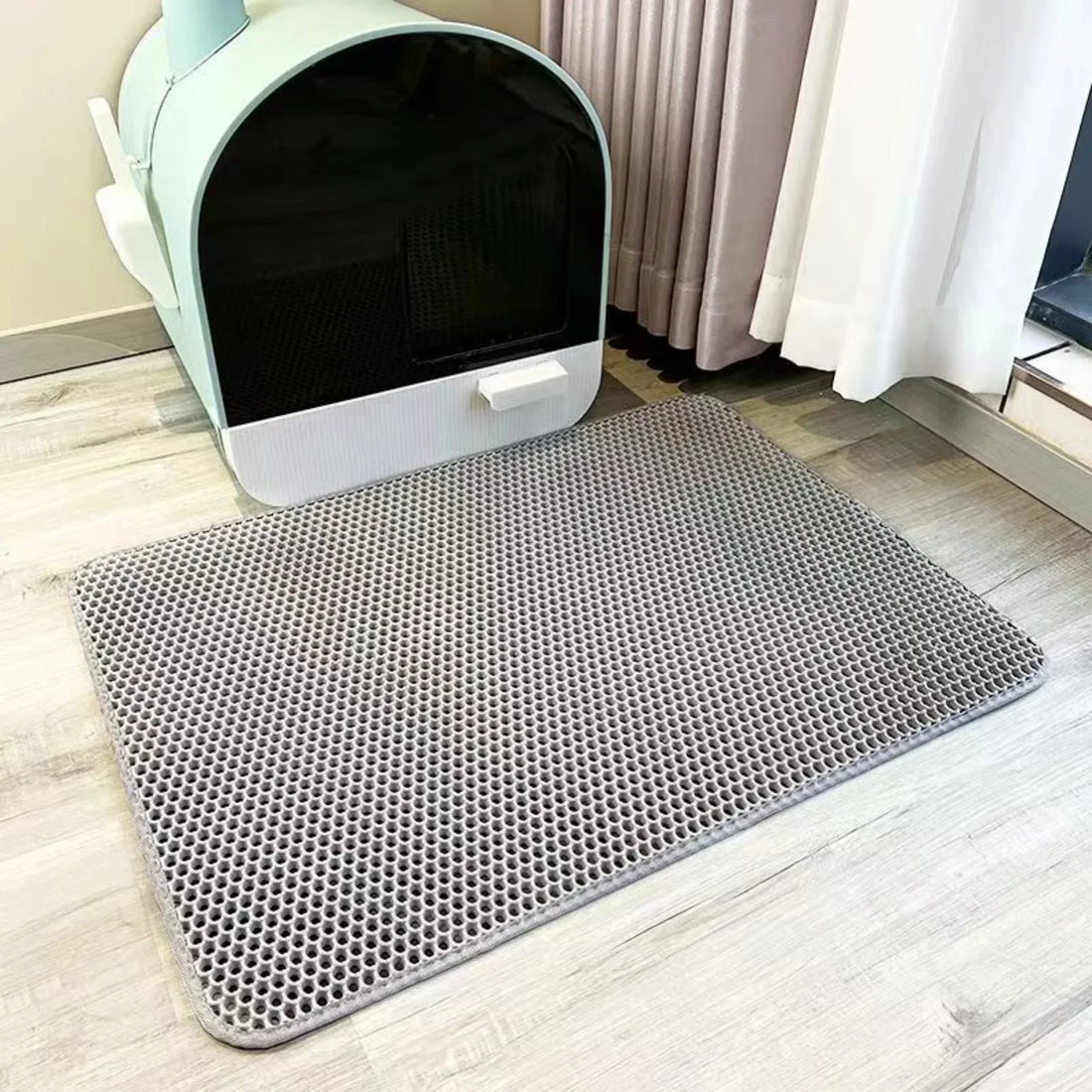 Tapis double couche gris en nid d'abeille posé à plat devant un bac à litière fermé