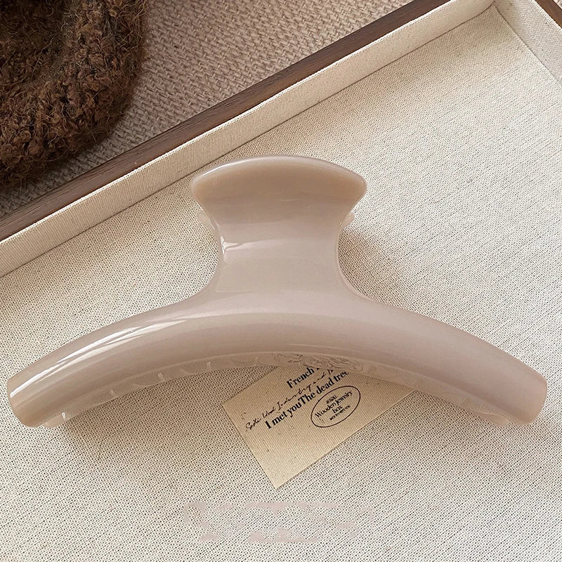 Grande pince à cheveux beige rosé posée sur une carte et un tissu crème