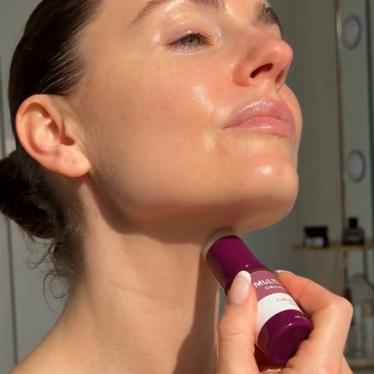 Femme qui glisse le bâton multi-baume prune sous la mâchoire, tête relevée